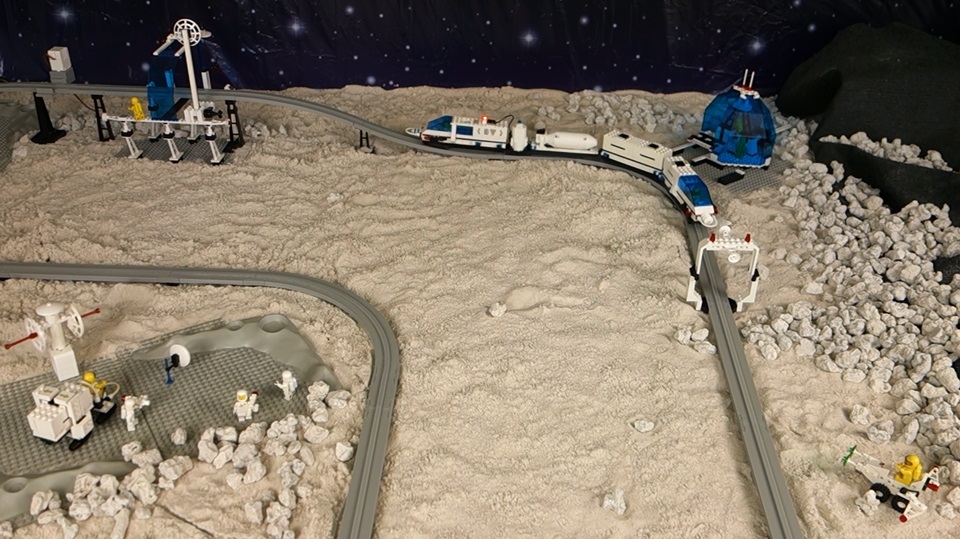 A LEGO futuron monorial train on 3D printed LEGO compatible monorail tracks in a moonscape.  The train has been extended with two 4DBrix monorial extension cars.